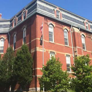 A historic brick building with a flagpole and trees in the foreground.