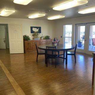 A spacious dining area with a table and chairs, featuring wooden flooring and large windows letting in natural light.