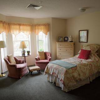 A cozy bedroom with a single bed, two armchairs by a window, and soft lighting.