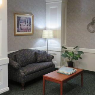 A cozy waiting room with a sofa, lamp, and table featuring a plant and artwork on the wall.