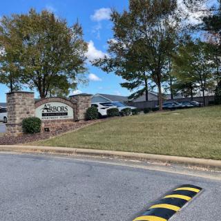 A scenic entrance with a sign, surrounded by trees and parked cars.