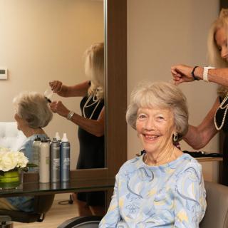 An elderly woman smiling while getting her hair styled in a salon.