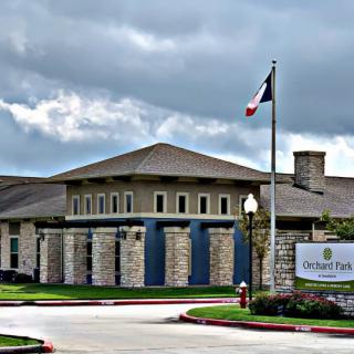 A modern building under a cloudy sky with a flag and signage at the entrance.
