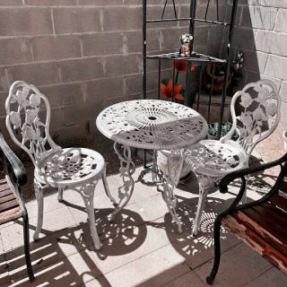 A quaint outdoor seating area featuring a white metal table and chairs, perfect for enjoying a sunny day.