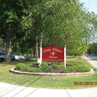 A decorative sign surrounded by landscaped greenery near a roadside.