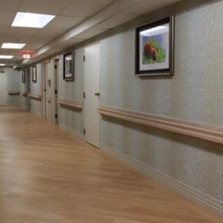 A quiet hospital hallway with beige walls and wood flooring.