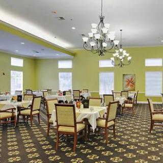 A spacious dining room with neatly arranged tables and chairs, featuring elegant chandeliers and a patterned carpet.