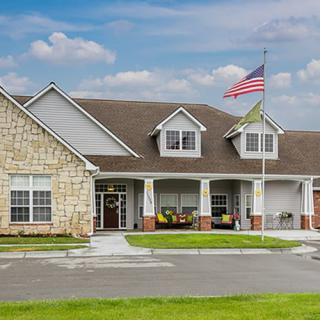 A charming house with an American flag flying, surrounded by a green lawn under a partly cloudy sky.