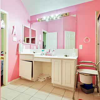 A bathroom with vibrant pink walls, a wide mirror above a white vanity, and tiled flooring.