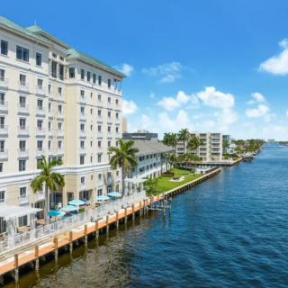 A beautiful waterfront hotel with palm trees and a scenic view of the river on a sunny day.
