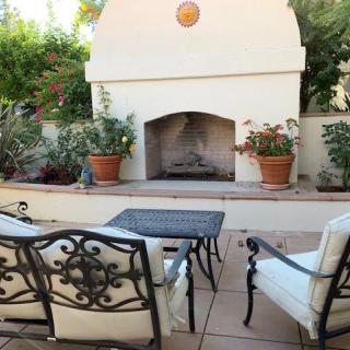 A cozy outdoor patio with a fireplace and comfortable seating surrounded by lush greenery.