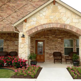 A welcoming front porch with a brick and stone exterior, adorned with flowers and seating.