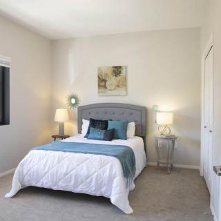 A modern, minimalist bedroom with a grey upholstered headboard, white bedding, teal accents, and elegant bedside lamps.