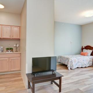 A cozy studio apartment featuring a small kitchenette and a bedroom with a TV.