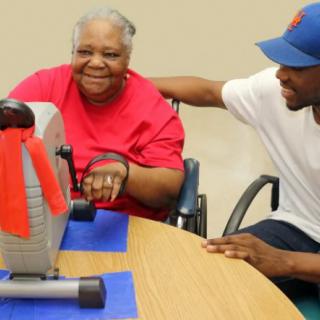 An elderly woman in a wheelchair interacts with a caregiver during a therapy session.