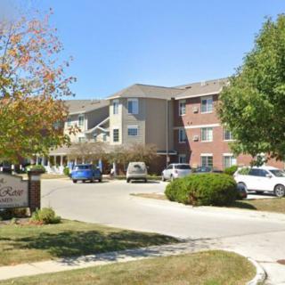 A suburban apartment building with a parking lot and trees in the foreground.