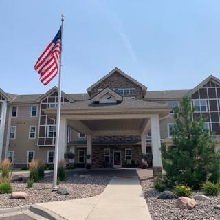 The image shows the entrance of a building with an American flag and well-maintained landscaping.