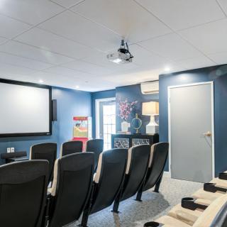 A small home theater room featuring multiple chairs, a large screen, and a ceiling-mounted projector set against blue walls.
