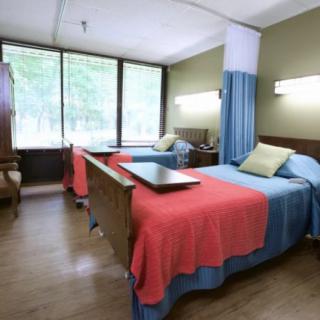 A hospital room with two beds, featuring colorful blankets and a large window providing natural light.