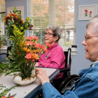 Two elderly individuals participate in a flower arranging activity at a care center.