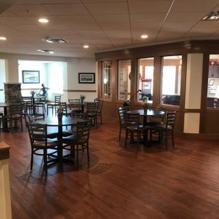 An empty dining area with wooden tables and chairs, featuring polished wood flooring.