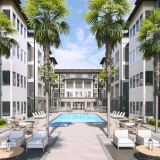 A luxurious apartment complex with a central swimming pool flanked by palm trees and modern buildings.
