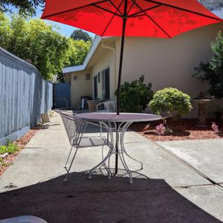 A cozy outdoor patio setup with a red umbrella, offering shade on a sunny day.