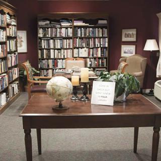 A cozy reading room with bookshelves filled with books, a globe on a wooden table, and comfortable chairs for reading.