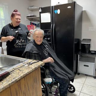 A caregiver is giving a haircut to a senior citizen in a cozy indoor setting.