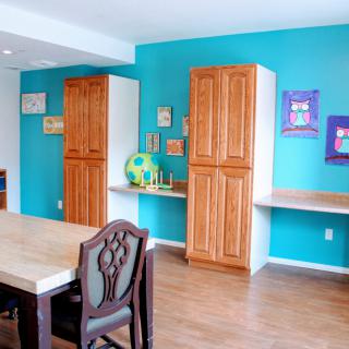 A colorful room with wooden furniture, including a table and chairs, cabinets, and artwork on the walls.