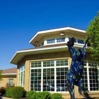 A modern building with large windows and a colorful horse sculpture in front.