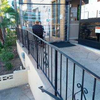A view of a patio area with decorative railings, steps leading up to a building, and some greenery in the background.