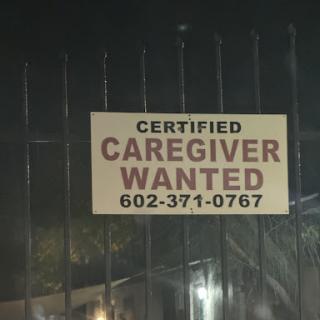 A sign indicating a job opening for a certified caregiver, illuminated at night.