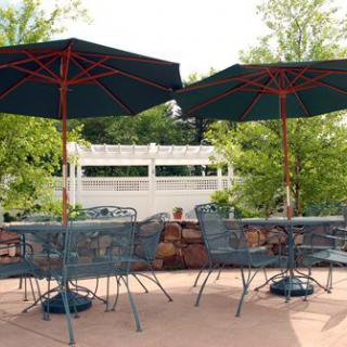 An outdoor patio area with tables and chairs under large umbrellas, surrounded by greenery.