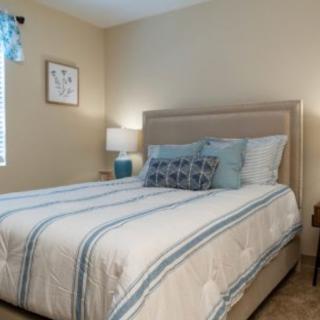 A cozy bedroom with a neatly made bed, featuring striped bedding and decorative pillows, accompanied by a lamp on the nightstand.
