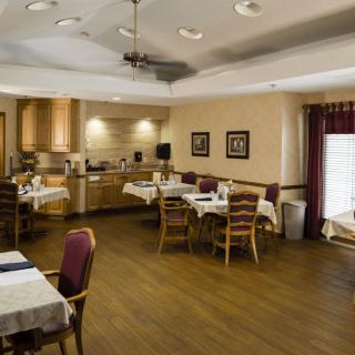 A cozy dining room with tables and chairs, adjacent to a small kitchen area.