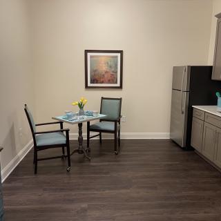 A small kitchen with a dining area, featuring a table set for two next to a refrigerator and artwork on the wall.