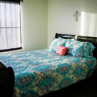 A cozy bedroom with a colorful bedding set and a window with sheer curtains, creating an inviting atmosphere.