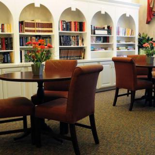 A cozy library space featuring shelves of books, comfortable chairs, and round tables adorned with flowers.