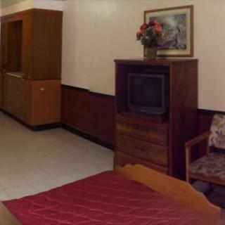 A hotel room with basic furnishings including a television, bed, and armchair.