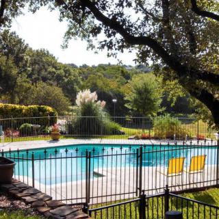 A serene outdoor swimming pool surrounded by lush greenery and set within a fenced area, featuring two bright yellow chairs for relaxation.