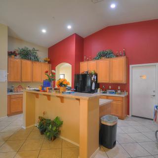 A modern kitchen with wood cabinetry and a red accent wall, featuring an island counter and recessed lighting.
