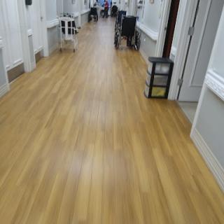 A view of a well-lit hallway with wooden flooring and furniture along the sides.