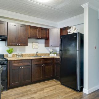 A modern kitchen featuring dark wood cabinets, a black refrigerator, and wooden flooring.