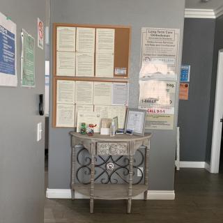 A view of an office hallway featuring a bulletin board filled with notices and a small table displaying pamphlets.