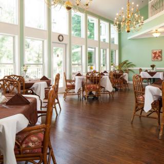 A bright and elegant restaurant dining area with large windows, chandeliers, and neatly arranged tables.