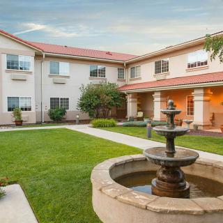 A picturesque courtyard featuring a central fountain surrounded by a neatly maintained lawn and a two-story building.