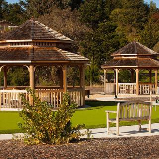A serene park setting featuring two wooden gazebos surrounded by greenery and a bench in the foreground.