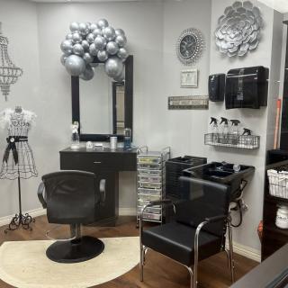 A stylish hair salon interior with a black styling chair, mirror, and silver balloon decorations.