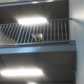 A view of an interior staircase with a balcony and overhead lighting.